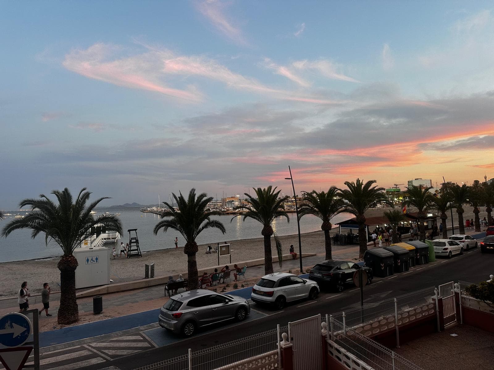 Uitzicht vanaf het balkon over de Mar Menor bij zonsondergang, met palmen langs de boulevard